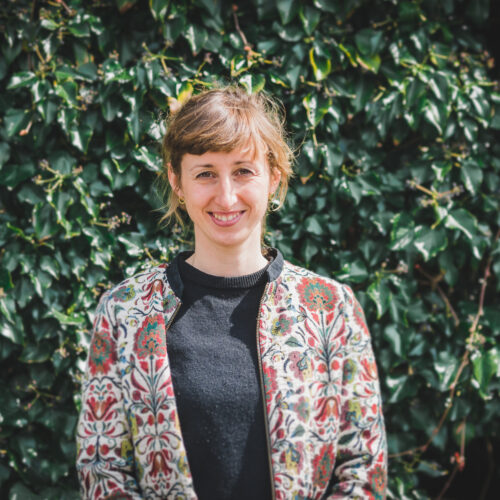Das Foto zeigt Selma Beck. Sie steht vor einer grünen Hecke.