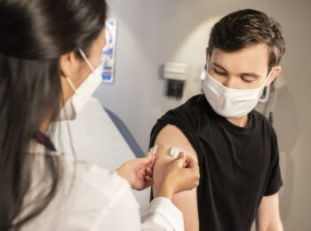 Das Foto zeigt eine Ärztin, die einen jungen Mann impft.