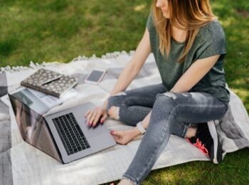 Foto einer Frau auf einer Decke mit Laptop und Schreibutensilien
